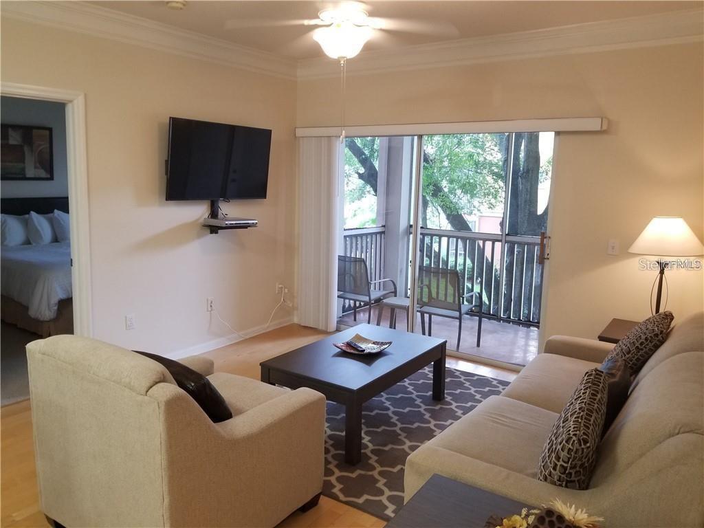 A living room features a sofa, armchair, coffee table, wall-mounted television, and a sliding glass door — 4207 S DALE MABRY HIGHWAY UNIT 10207, TAMPA, FL
