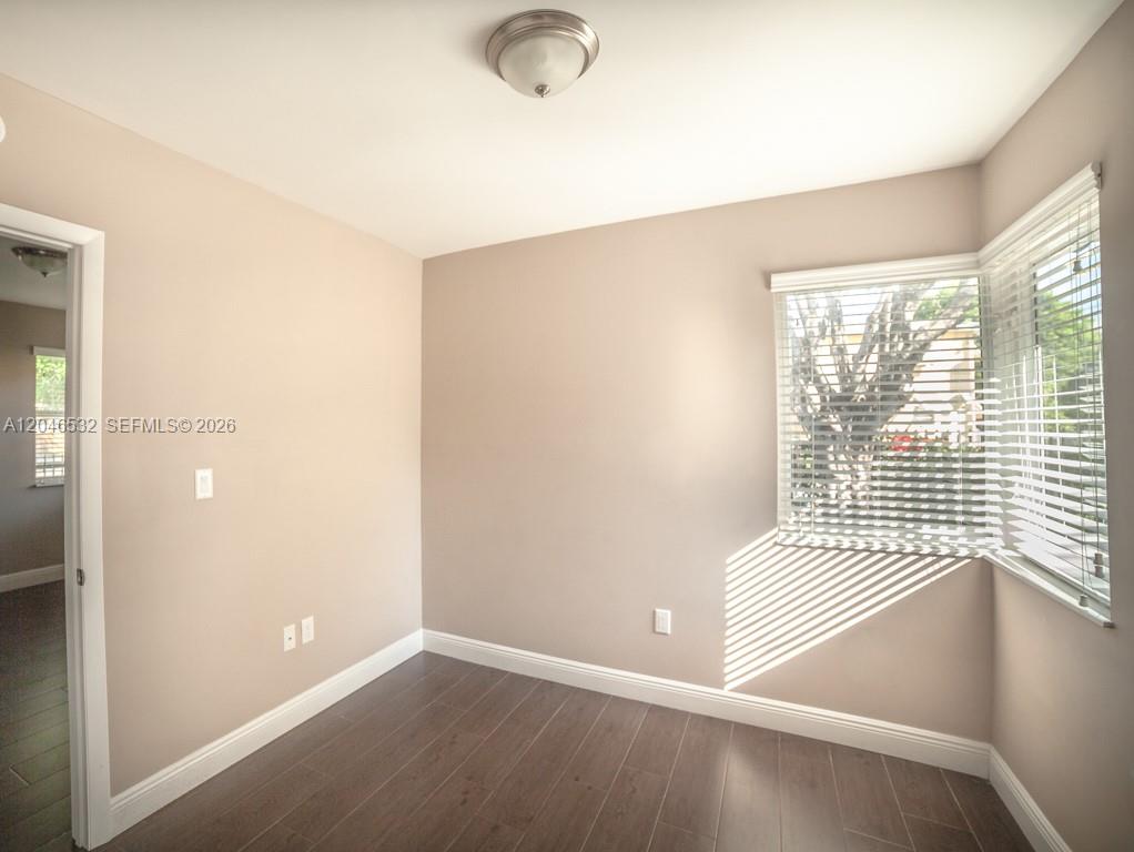 An empty room features dark wood-look flooring, light-colored walls, and a corner window with blinds — 500 SW 9th Ave # 1, Miami FL 33130, MIAMI, FL