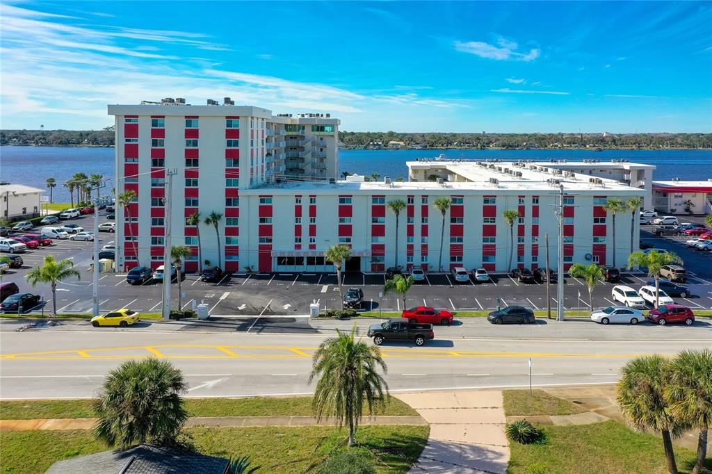 An aerial view shows a multi-story apartment building with red accents next to a river — 2711 N HALIFAX AVENUE UNIT 370, DAYTONA BEACH, FL