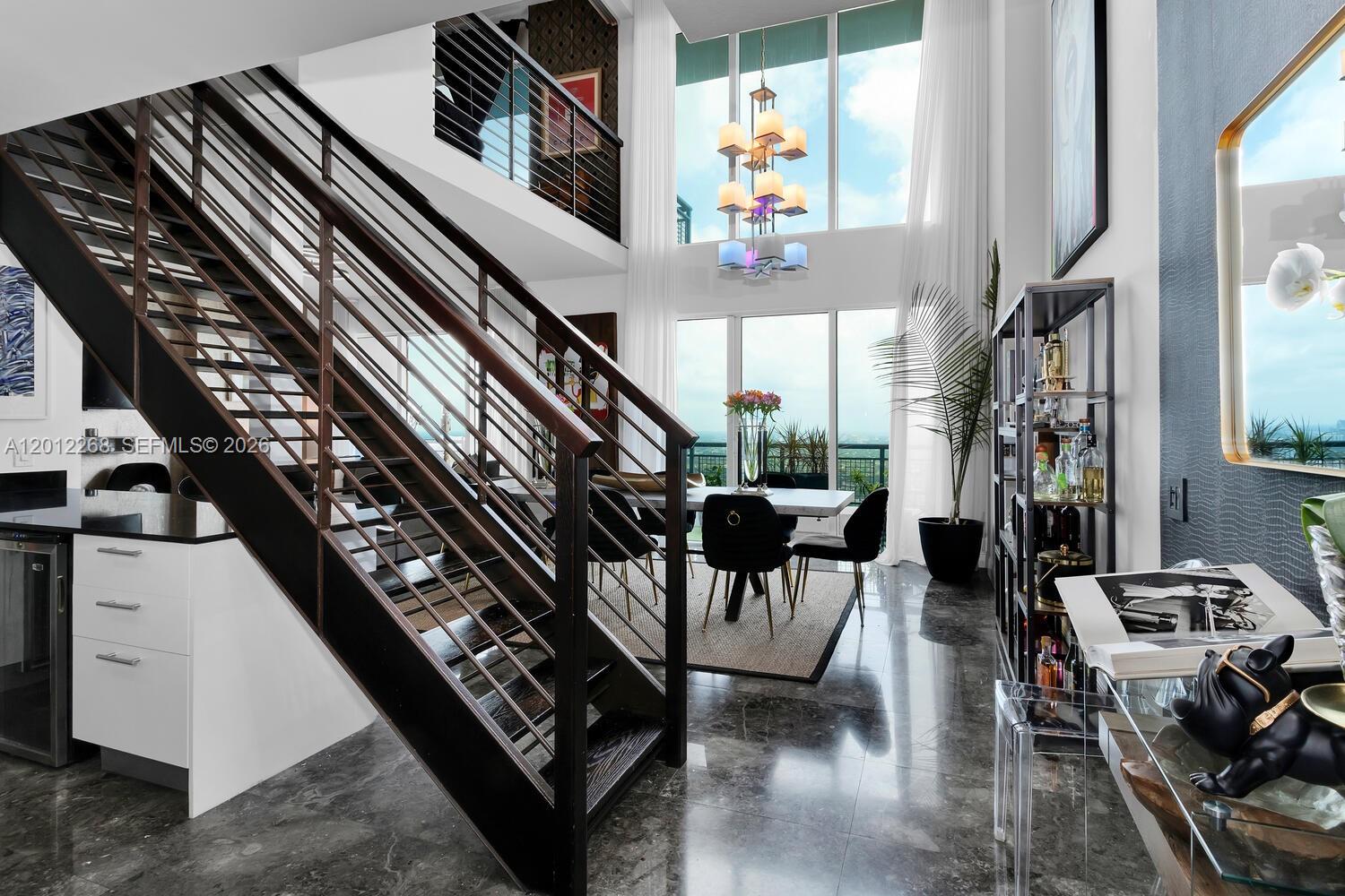 A modern dining area features a staircase, floor-to-ceiling windows, and a multi-tiered chandelier — 60 SW 13th St # 4005, Miami FL 33130, MIAMI, FL