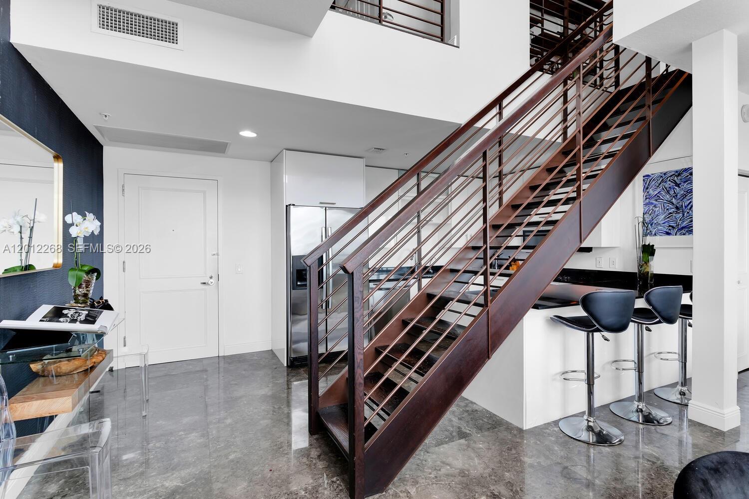A modern kitchen features a dark wood staircase, stainless steel appliances, and gray tile flooring — 60 SW 13th St # 4005, Miami FL 33130, MIAMI, FL