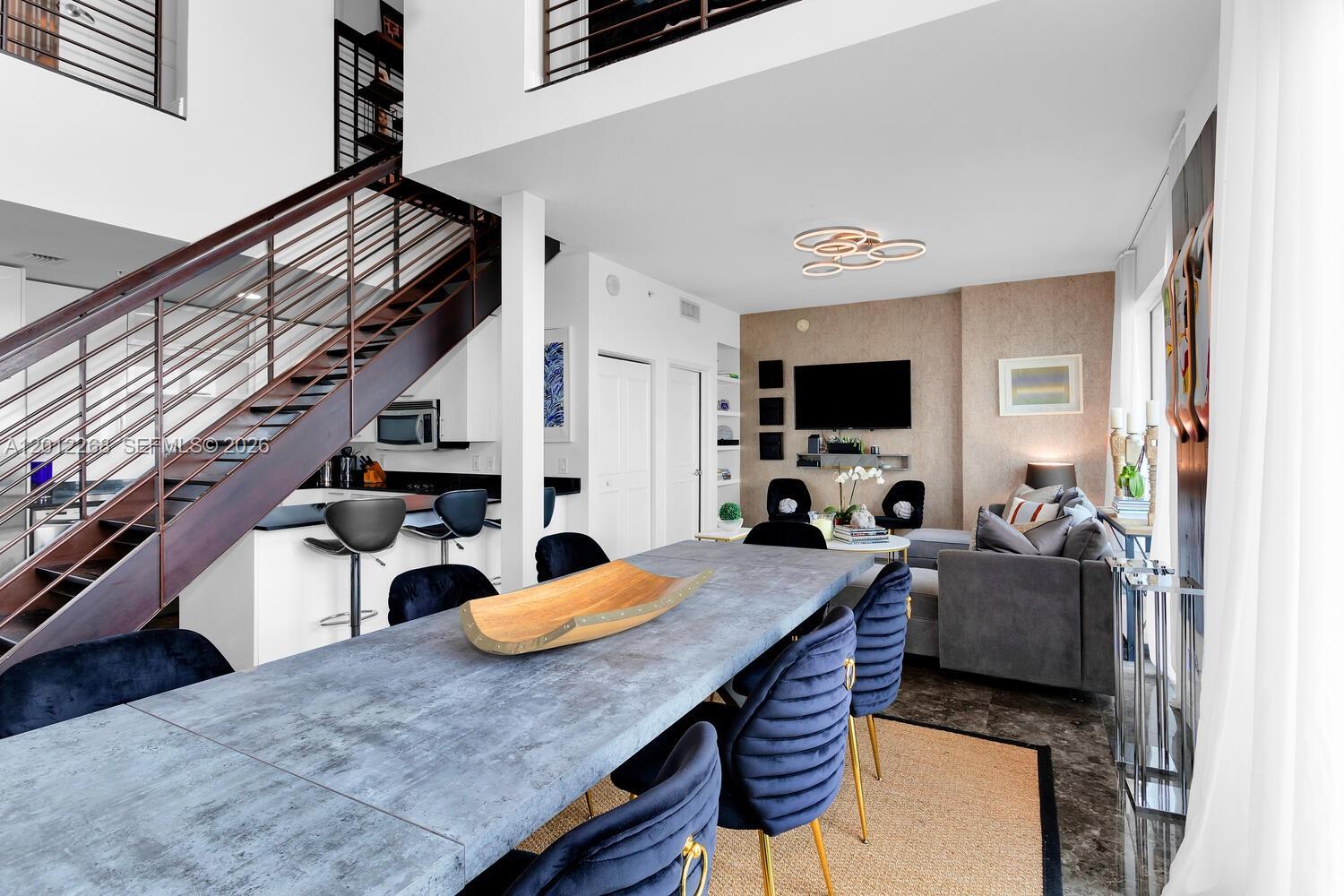 A modern open-plan living and dining area features a staircase, gray table, and blue chairs — 60 SW 13th St # 4005, Miami FL 33130, MIAMI, FL