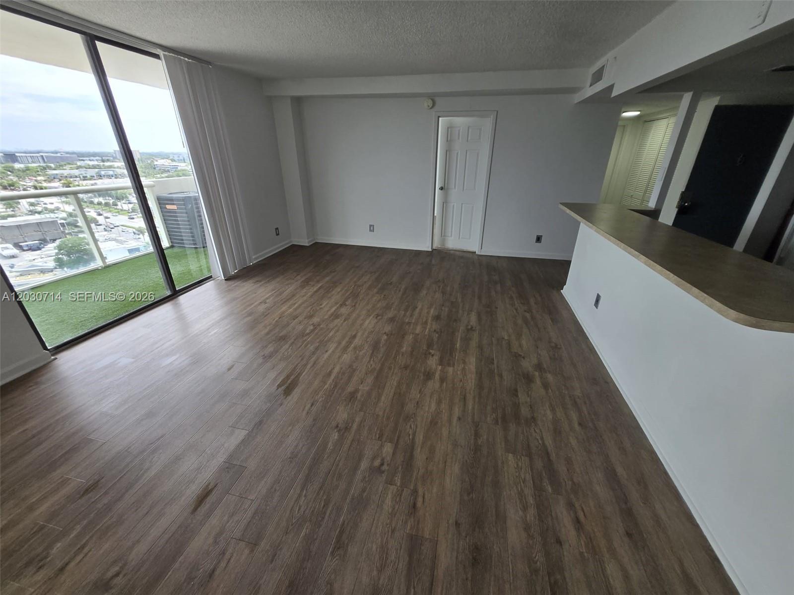 An empty living area features wood-look flooring, a breakfast bar, and a balcony with turf — NORTH MIAMI, FL