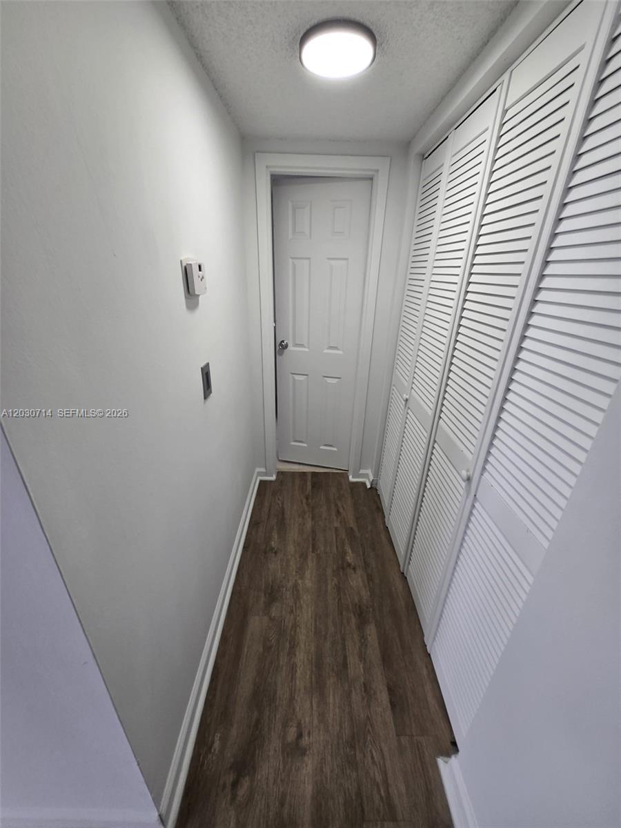 A narrow hallway features wood-look flooring, white walls, a ceiling light, and louvered closet doors — NORTH MIAMI, FL