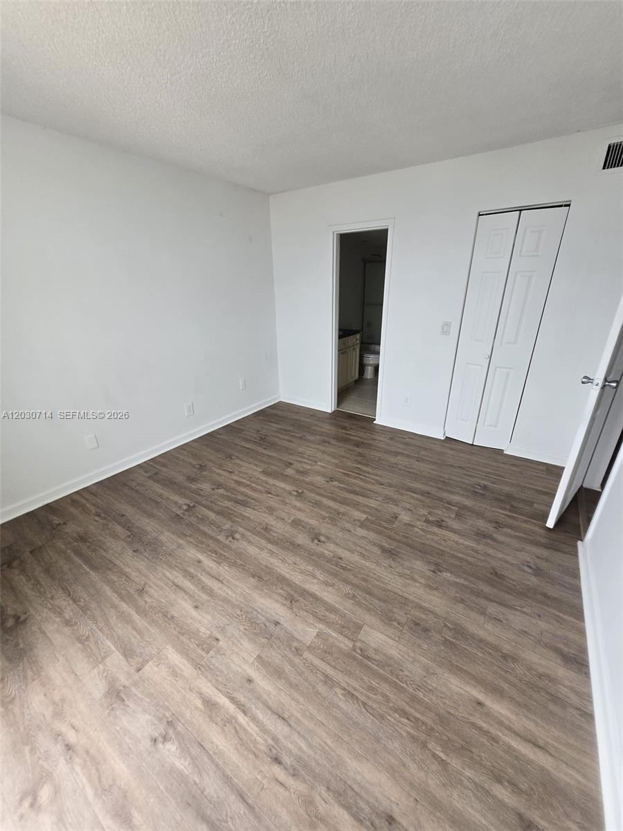 An empty bedroom features wood-look flooring, white walls, a closet, and an attached bathroom — NORTH MIAMI, FL