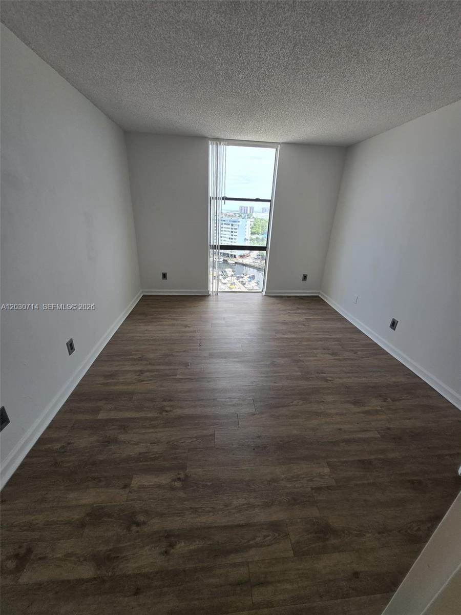 An empty room features wood-look flooring, white walls, and a window overlooking a marina — NORTH MIAMI, FL