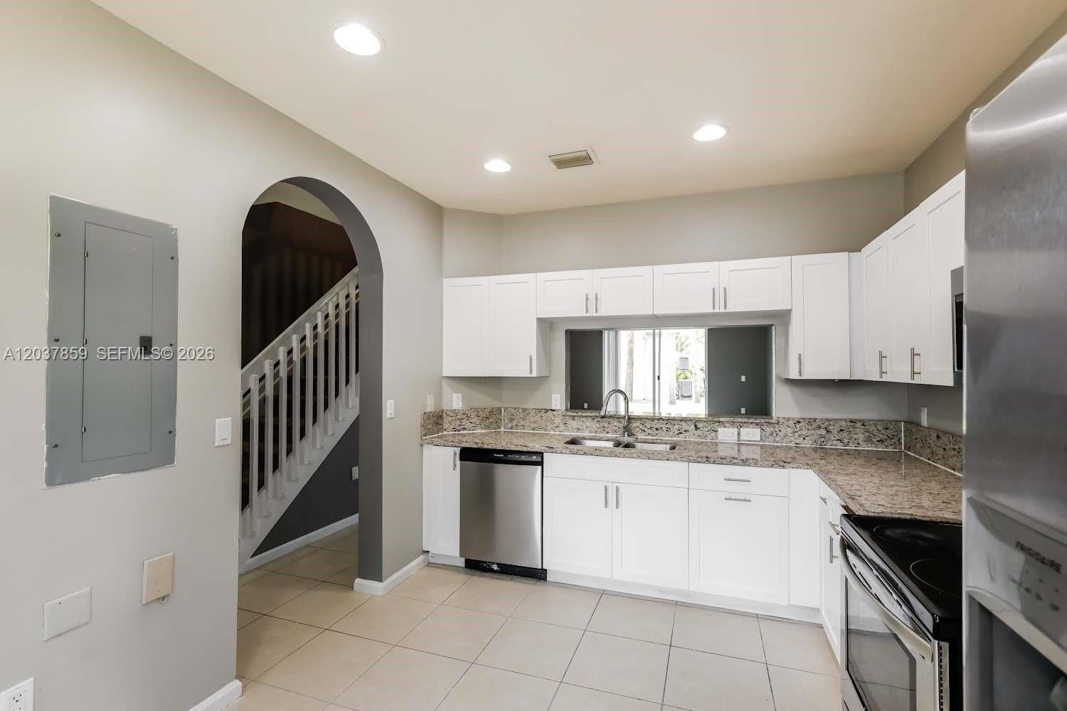 A kitchen features white cabinets, granite countertops, stainless steel appliances, and an arched entryway — MIRAMAR, FL