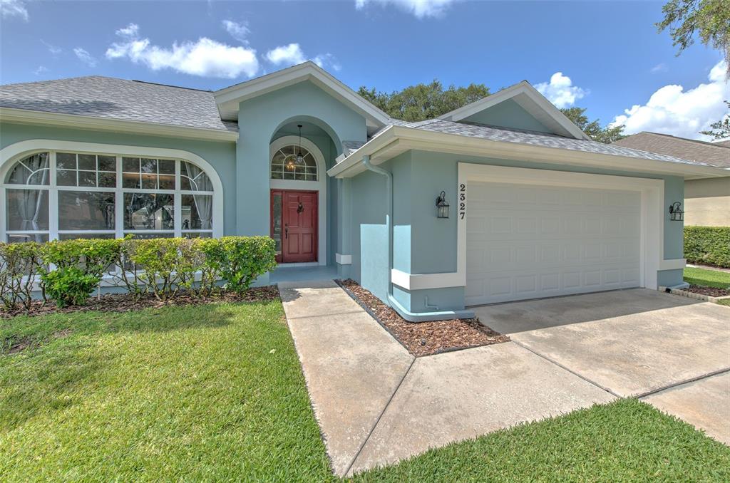 A light blue single-story house features a red front door, arched entryway, and two-car garage — 2327 EAGLE BLUFF DRIVE, VALRICO, FL