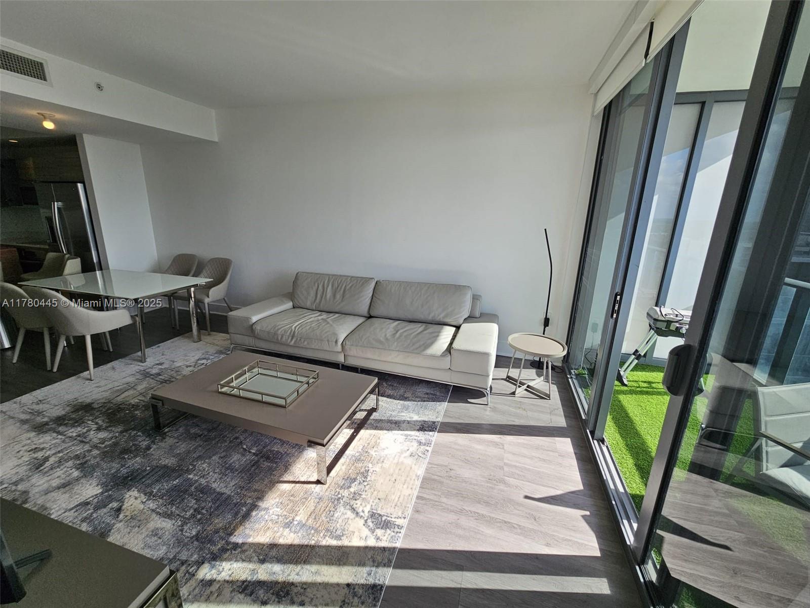 A living room with a grey sofa, coffee table, and sliding doors leading to a balcony — 121 NE 34 ST # 2511, Miami FL 33137, MIAMI, FL