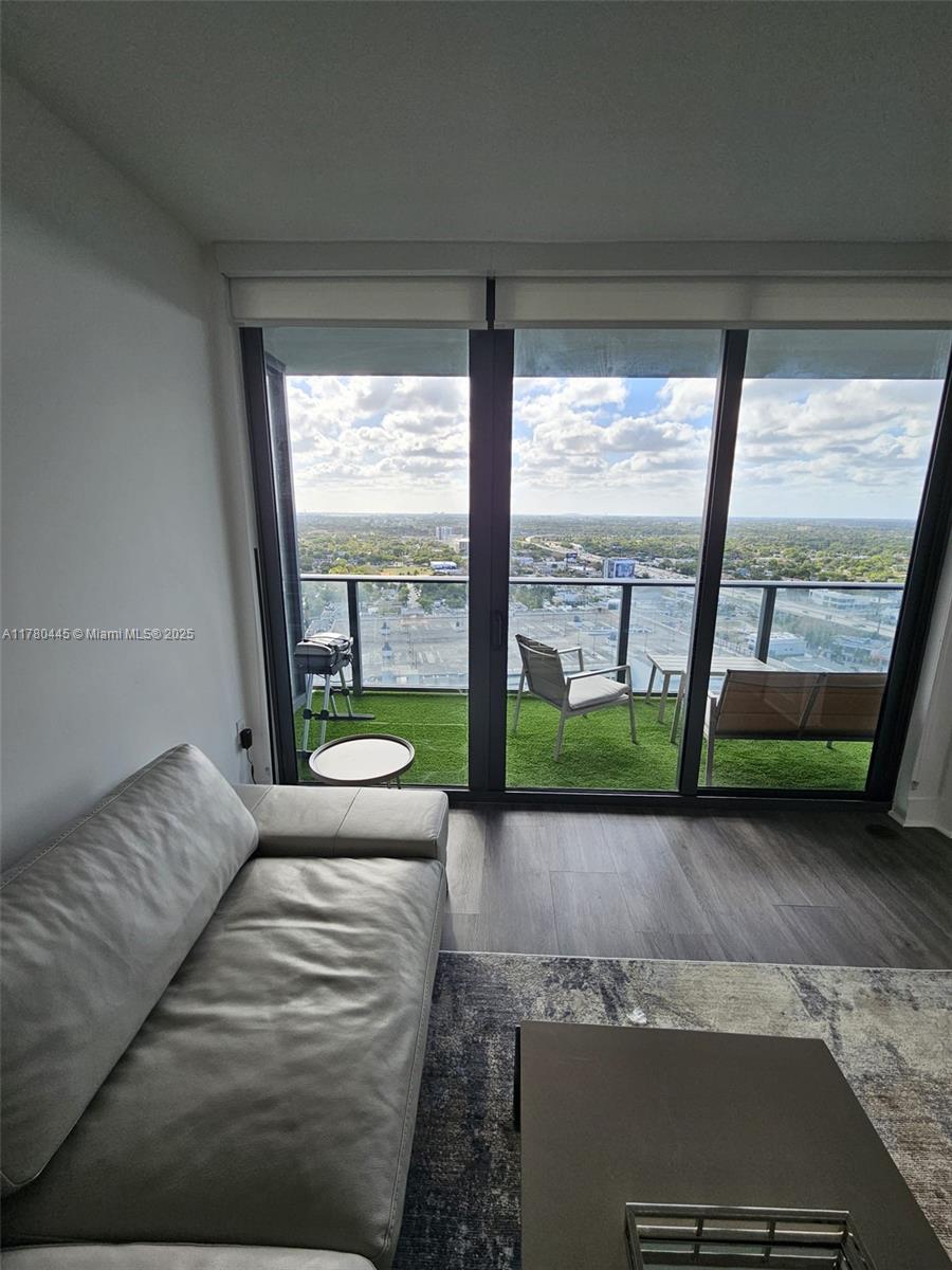 A living room with a gray sofa opens onto a balcony featuring artificial grass flooring — 121 NE 34 ST # 2511, Miami FL 33137, MIAMI, FL