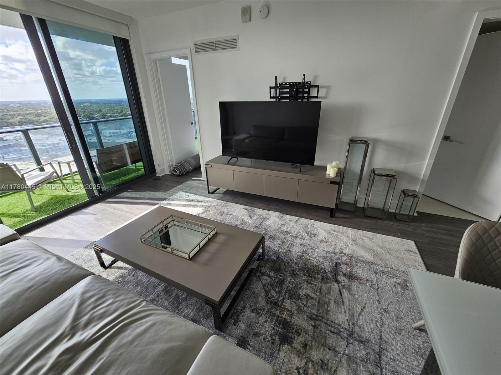 A modern living room features a television console, area rug, and a balcony with views — 121 NE 34 ST # 2511, Miami FL 33137, MIAMI, FL