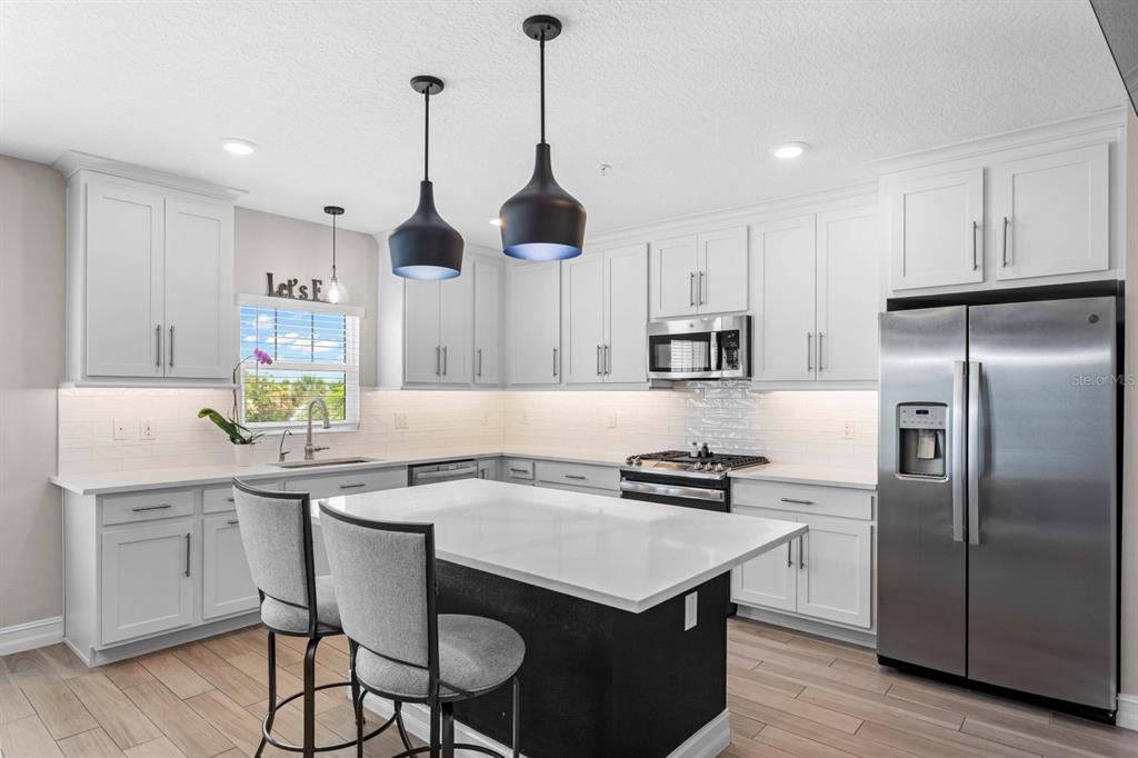 A modern kitchen features white cabinetry, a dark kitchen island, and stainless steel appliances — 5351 BRIDGE STREET UNIT 42, TAMPA, FL