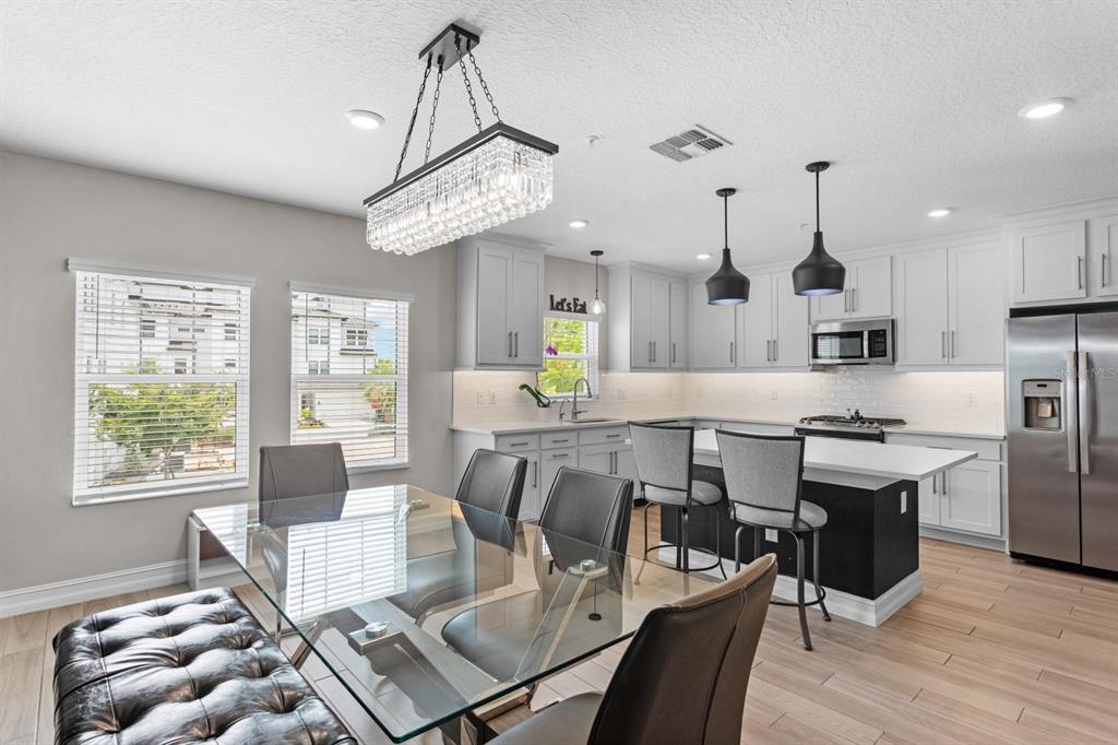 A modern kitchen and dining area with white cabinets, a glass table, and pendant lighting — 5351 BRIDGE STREET UNIT 42, TAMPA, FL