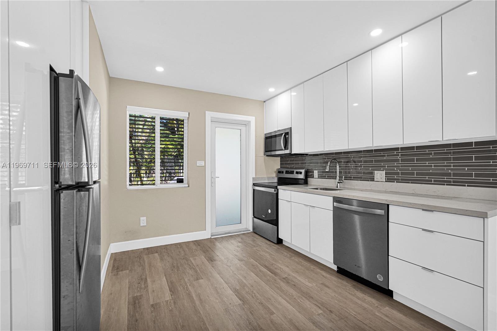 A modern kitchen features white cabinets, stainless steel appliances, and a gray tiled backsplash — 11919 NE 8th av, Biscayne Park FL 33161, BISCAYNE PARK, FL