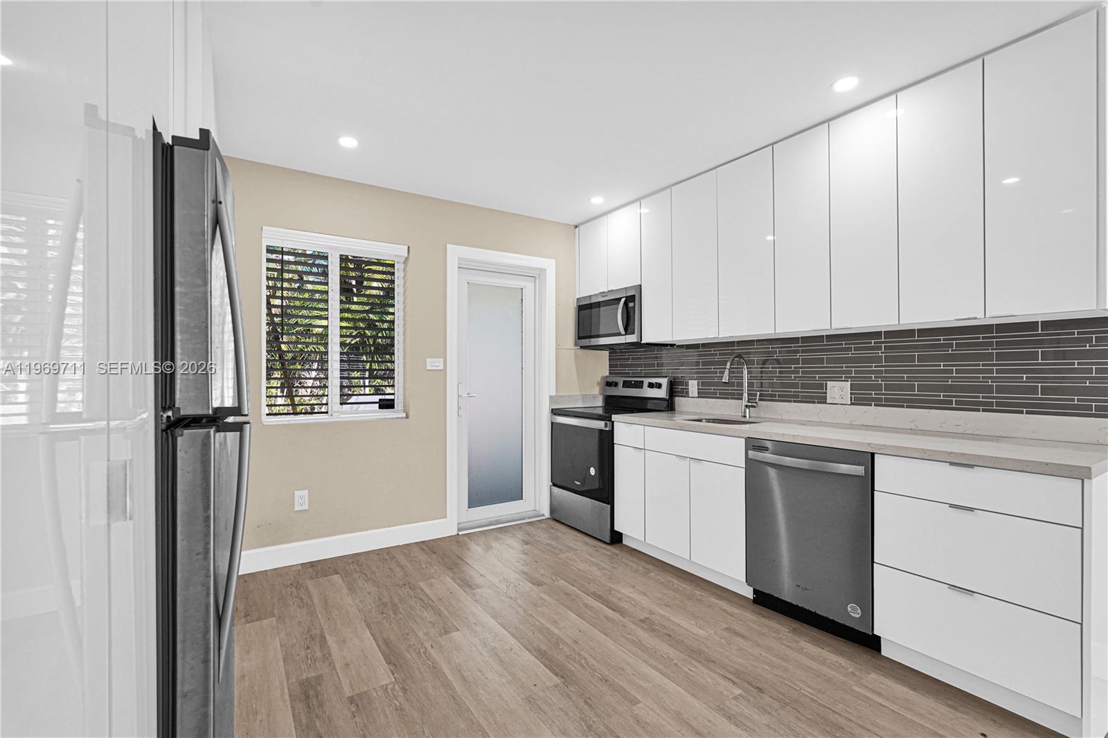 A kitchen features white flat-panel cabinets, stainless steel appliances, and a gray tiled backsplash — 11919 NE 8th av, Biscayne Park FL 33161, BISCAYNE PARK, FL