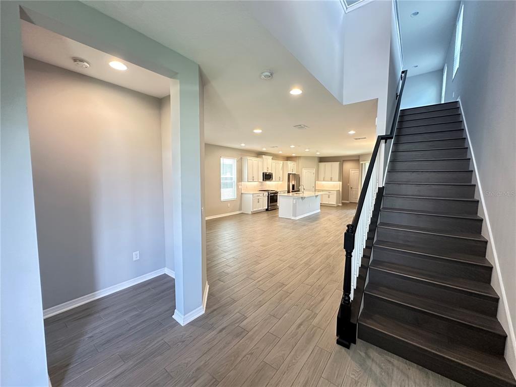 An open-concept living area features a staircase with dark wood treads and a white kitchen — 12513 ENCORE AT OVATION WAY, WINTER GARDEN, FL