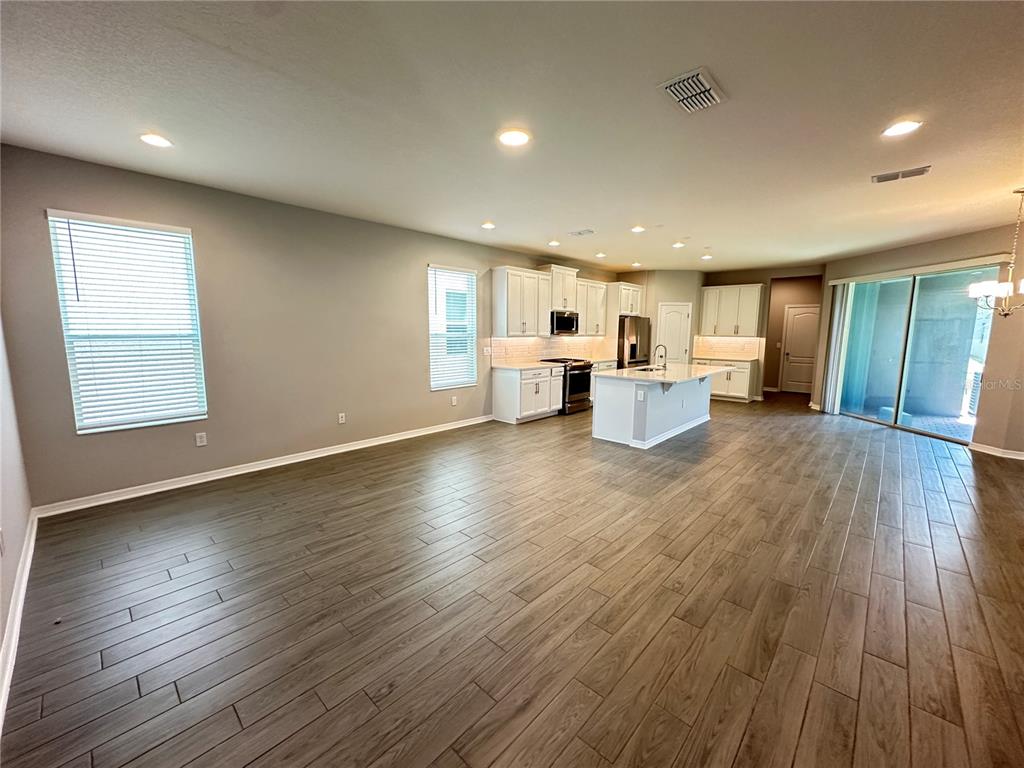 An open-concept kitchen and living area features wood-look tile flooring and white cabinetry — 12513 ENCORE AT OVATION WAY, WINTER GARDEN, FL