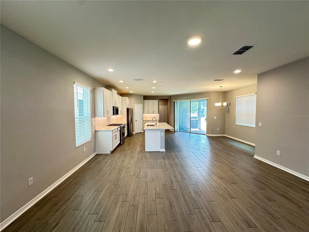 An open-concept kitchen and living area features white cabinetry, a center island, and wood-look flooring — 12513 ENCORE AT OVATION WAY, WINTER GARDEN, FL
