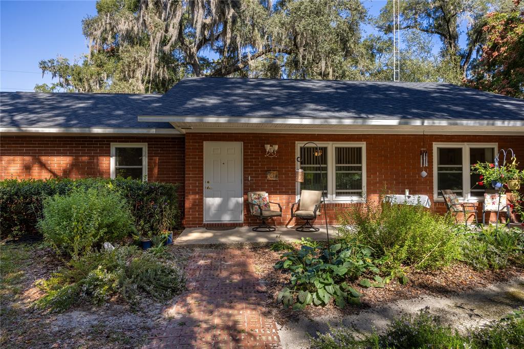 A single-story red brick house features a front porch, a brick walkway, and mature trees — 11440 SW ARCHER ROAD, GAINESVILLE, FL