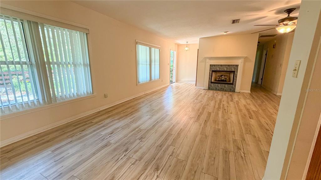 A living room with light wood-look flooring, a fireplace, and large windows with blinds — 11440 SW ARCHER ROAD, GAINESVILLE, FL