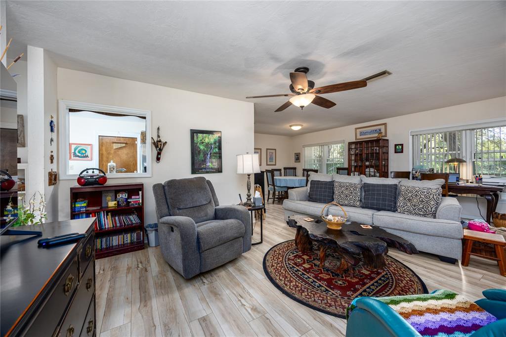 A living room features light wood-look flooring, a gray sofa, a recliner, and a ceiling fan — 11440 SW ARCHER ROAD, GAINESVILLE, FL