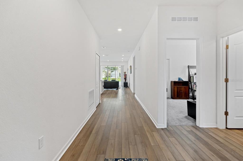 A hallway with wood-look flooring leads to a living area with a sliding glass door — 33 RIDGE ROAD, PALM COAST, FL
