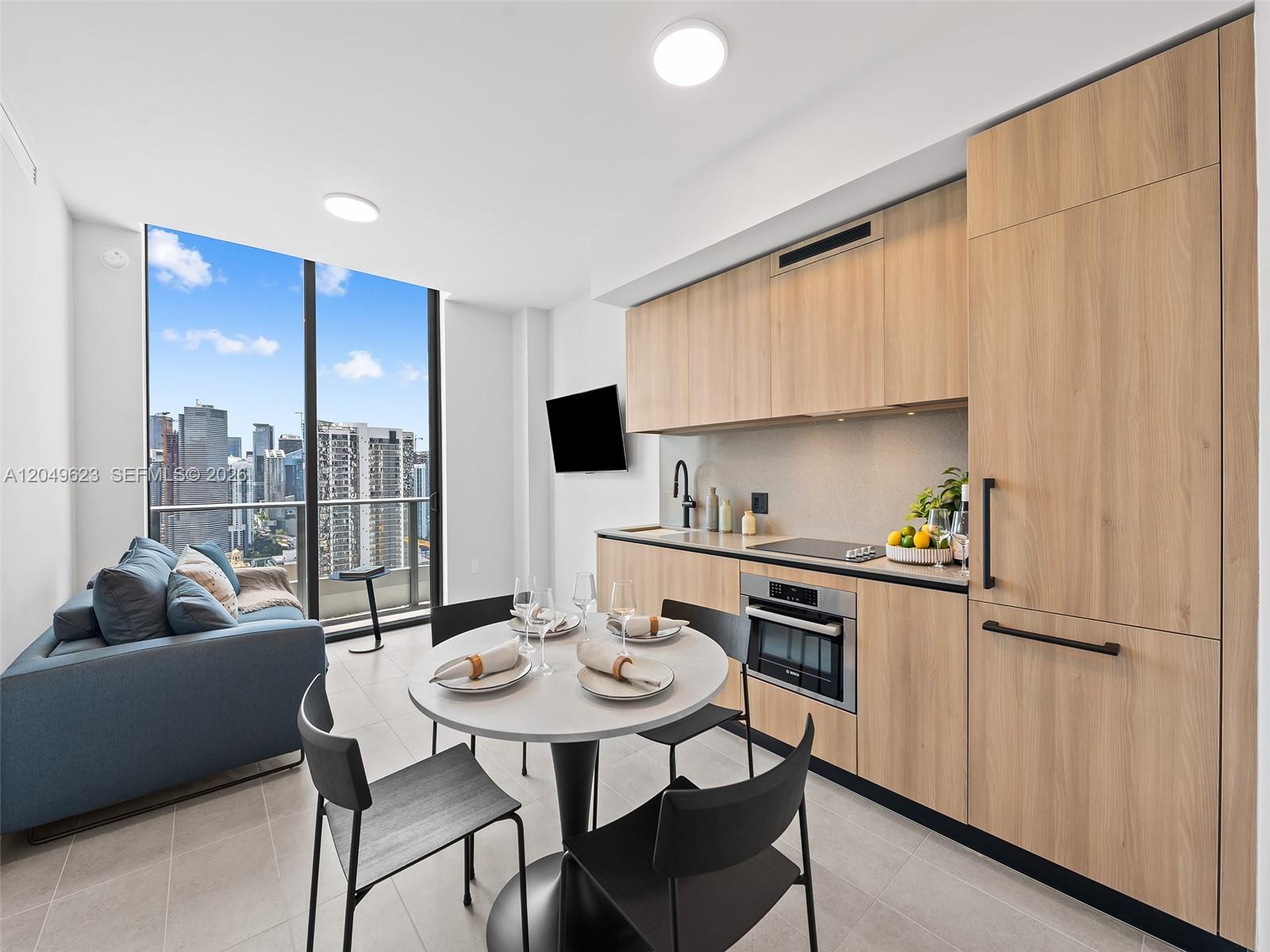 A modern studio apartment features a kitchenette with light wood cabinets, a dining table, and city views — 121 NE 5th St # 3703, Miami FL 33132, MIAMI, FL