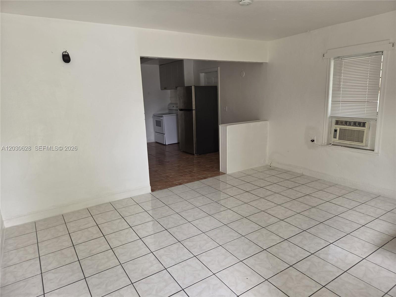 A room with white tiled floors and walls leads into a kitchen with dark appliances — 5605 Taylor St # 1, Hollywood FL 33021, HOLLYWOOD, FL