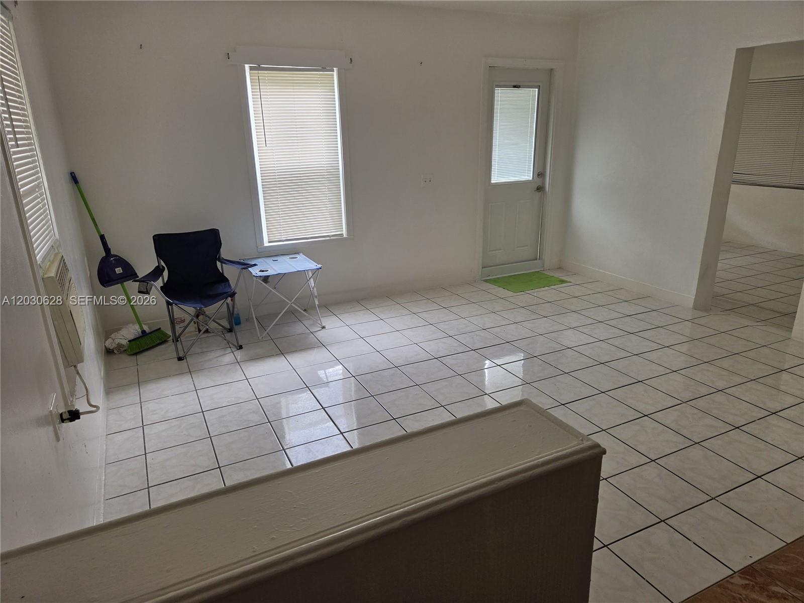 An empty room features white walls, white tiled floors, a window, and a door — 5605 Taylor St # 1, Hollywood FL 33021, HOLLYWOOD, FL