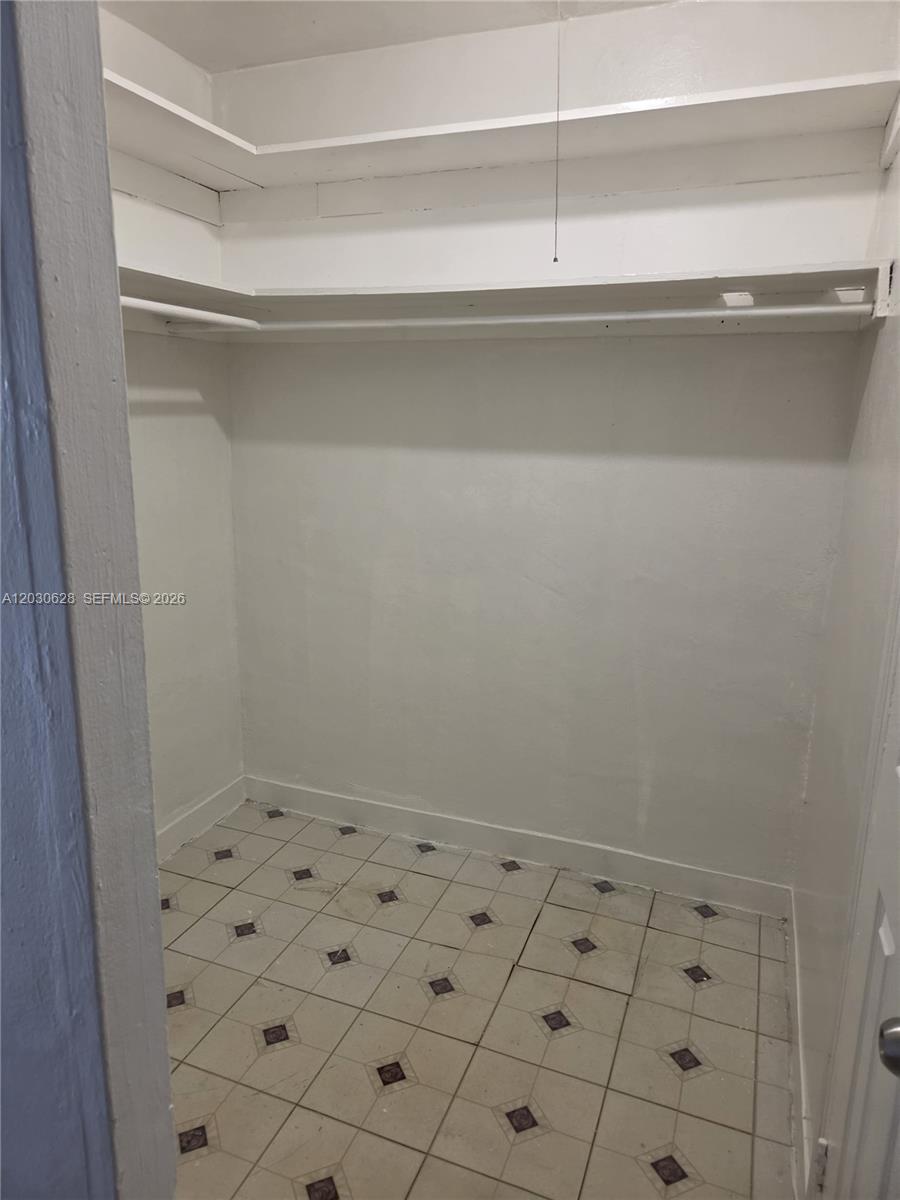 A walk-in closet features white shelving, a hanging rod, and light-colored square floor tiles — 5605 Taylor St # 1, Hollywood FL 33021, HOLLYWOOD, FL