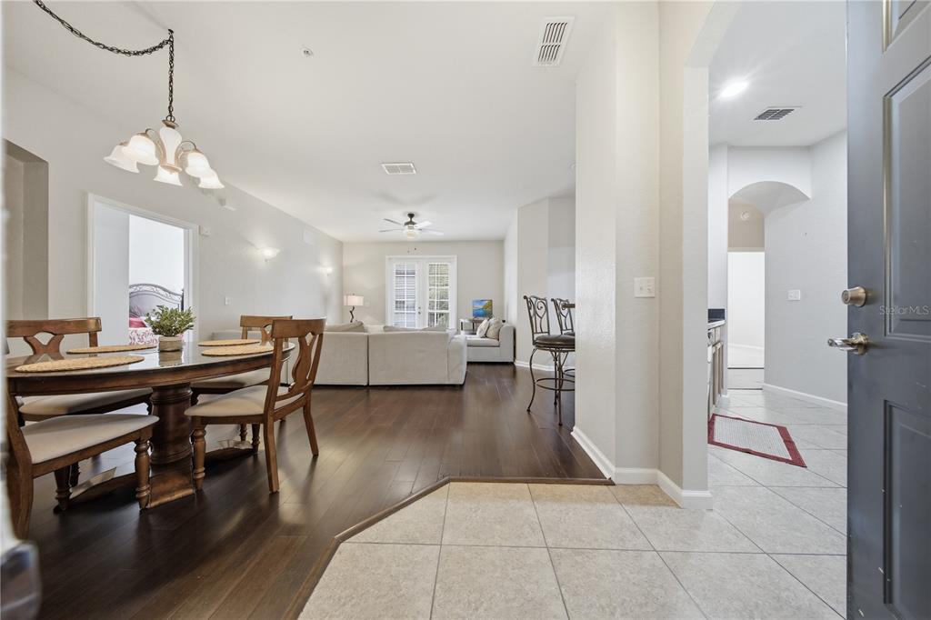 An open-concept living and dining area features dark wood flooring, a chandelier, and tile entry — 3001 LAUREL RUN LANE UNIT 204, KISSIMMEE, FL