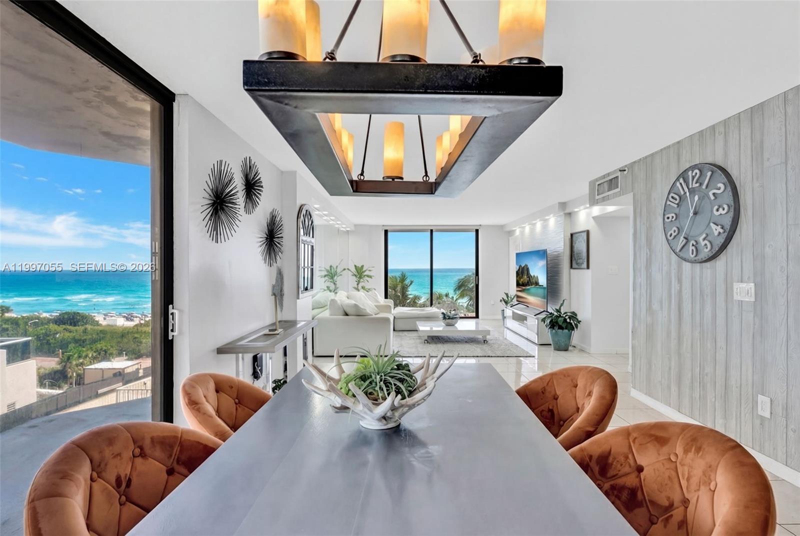 A dining area with orange tufted chairs overlooks an oceanfront living room and balcony — 6061 Collins Ave # 5F, Miami Beach FL 33140, MIAMI BEACH, FL