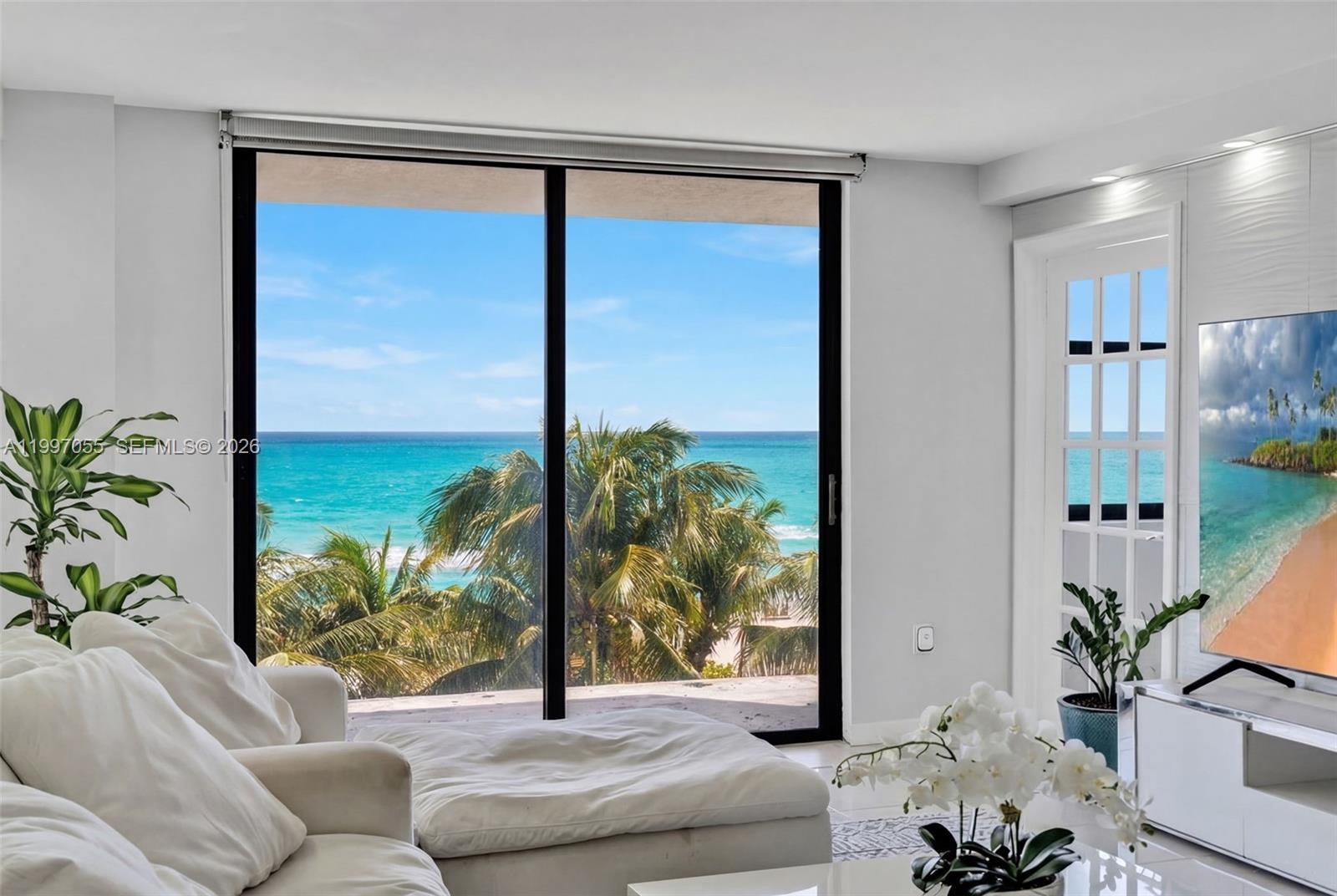 A bright living room features a white sofa, a television, and sliding doors overlooking the ocean — 6061 Collins Ave # 5F, Miami Beach FL 33140, MIAMI BEACH, FL