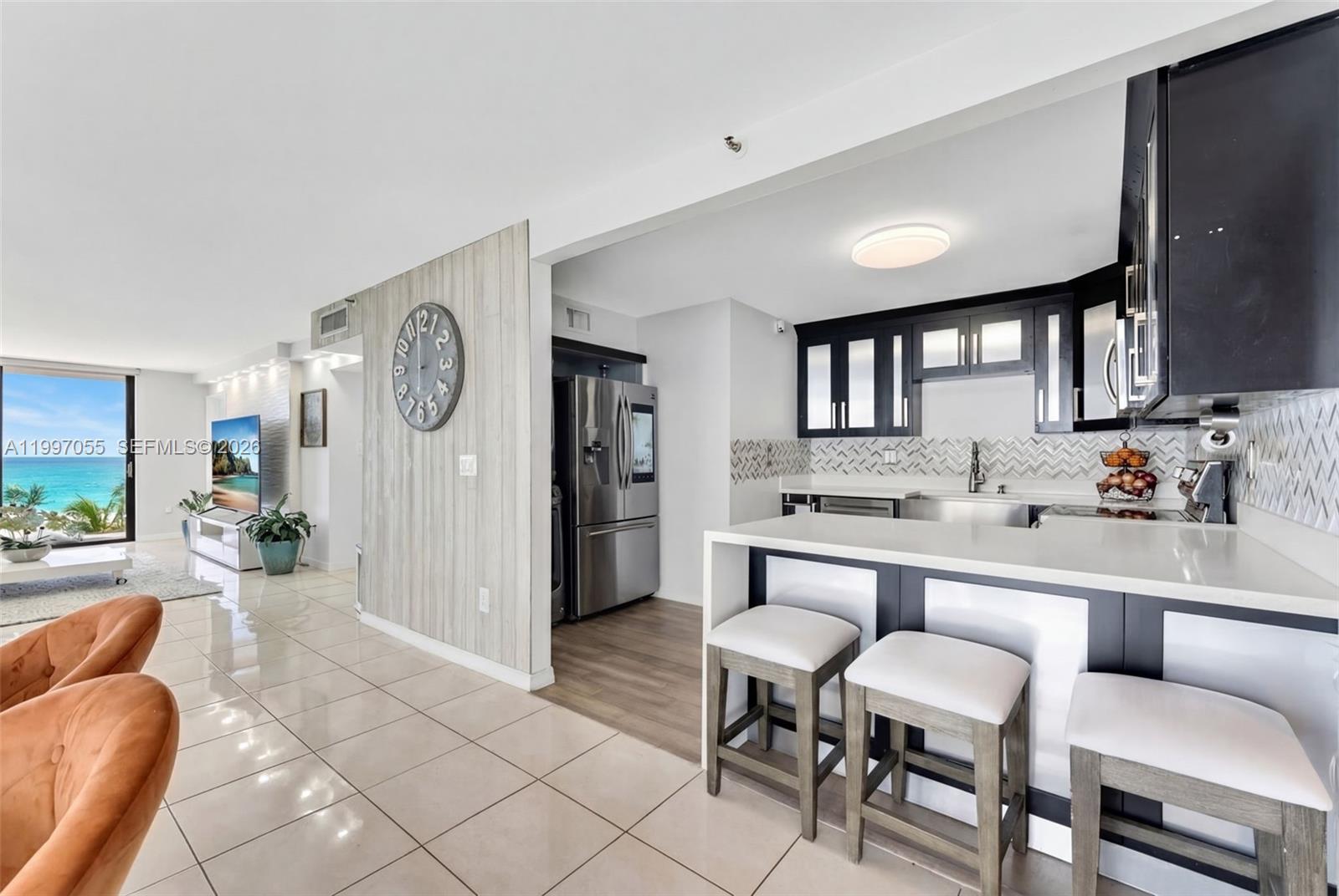 A modern kitchen with dark cabinets and a breakfast bar overlooks a living area — 6061 Collins Ave # 5F, Miami Beach FL 33140, MIAMI BEACH, FL