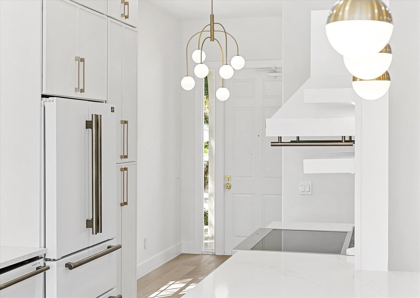A modern white kitchen features gold light fixtures, stainless steel appliances, and light wood flooring — 4789 Valencia Drive, Delray Beach FL 33445, DELRAY BEACH, FL