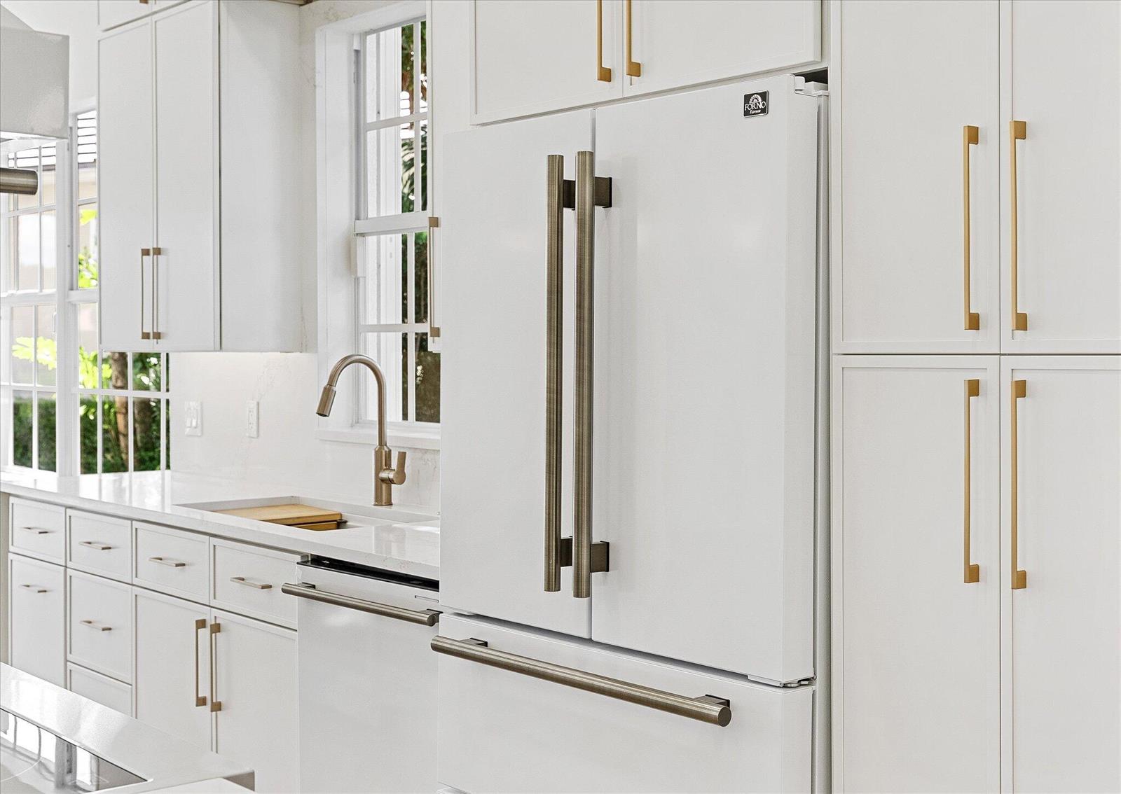 A white kitchen features a modern refrigerator, gold cabinet hardware, and a stainless steel faucet — 4789 Valencia Drive, Delray Beach FL 33445, DELRAY BEACH, FL