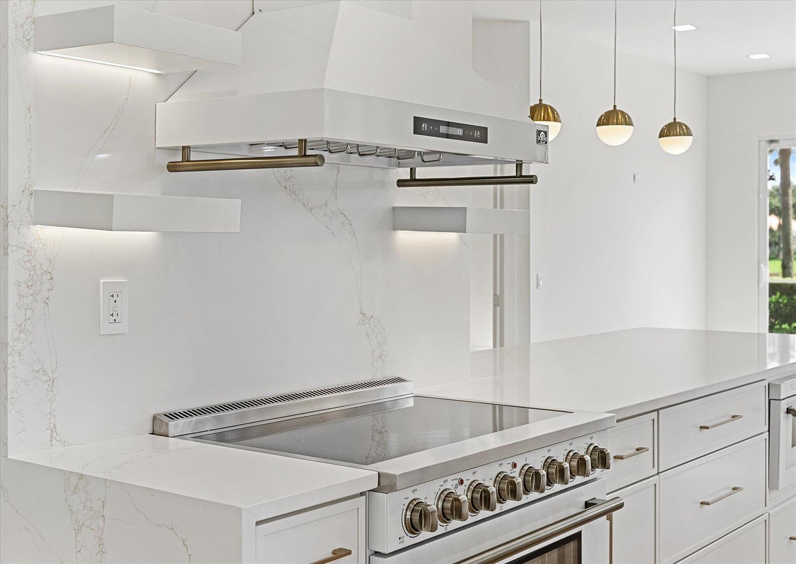 A modern kitchen features a white range hood, marble backsplash, and gold-toned hardware — 4789 Valencia Drive, Delray Beach FL 33445, DELRAY BEACH, FL