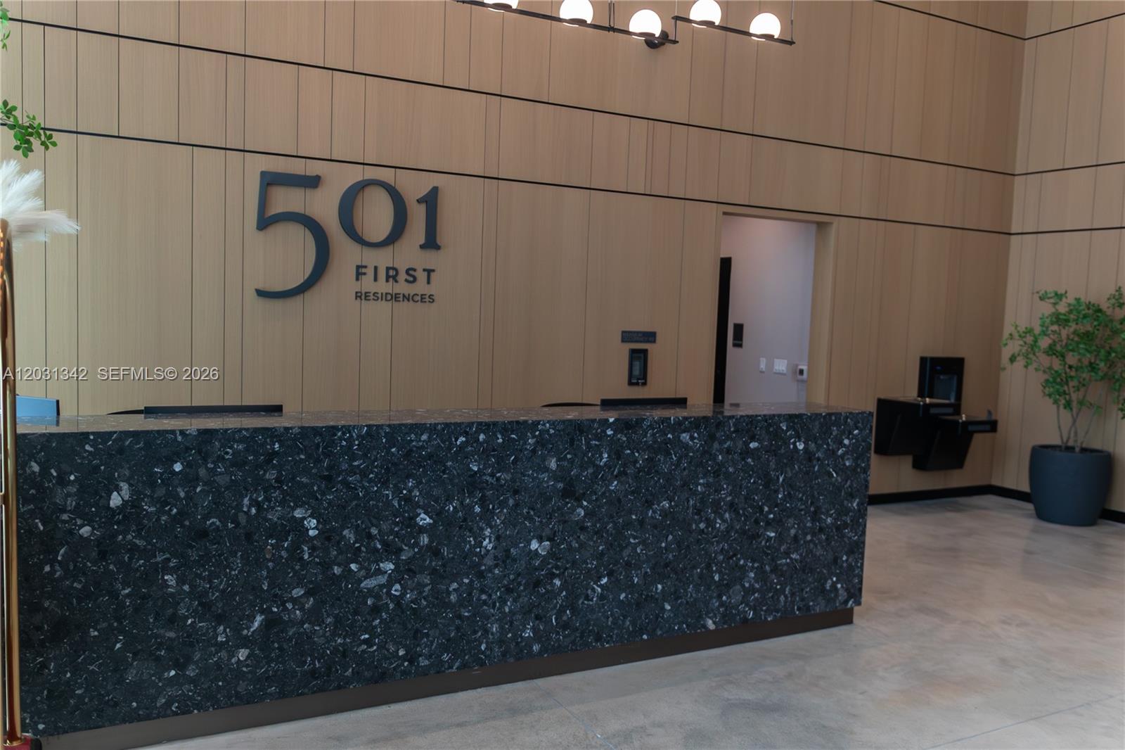 A modern lobby features a dark stone reception desk against a wood-paneled wall — 121 NE 5th St # 1012A, Miami FL 33132, MIAMI, FL