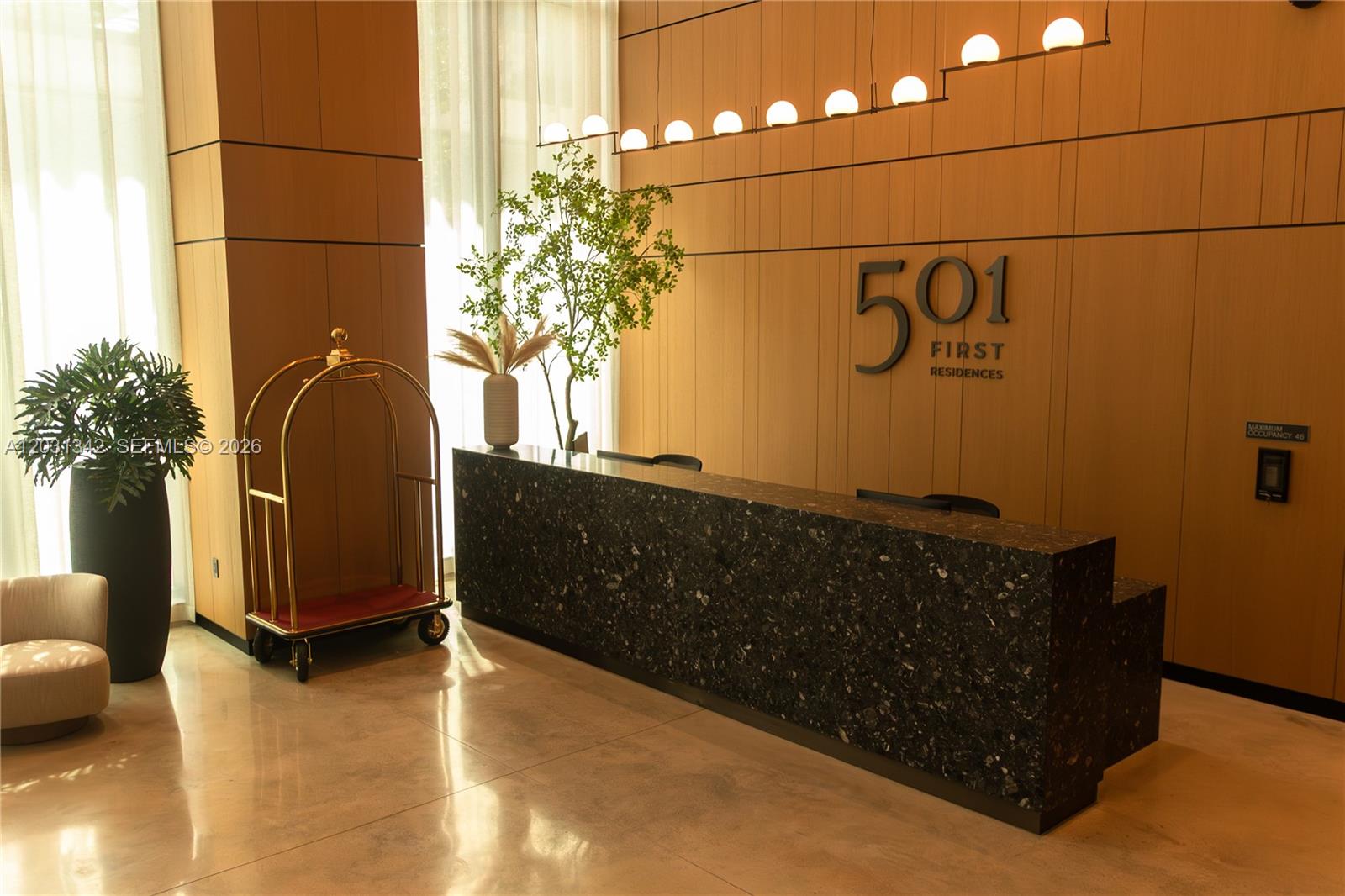 A modern lobby features a dark stone reception desk, wood-paneled walls, and a gold luggage cart — 121 NE 5th St # 1012A, Miami FL 33132, MIAMI, FL