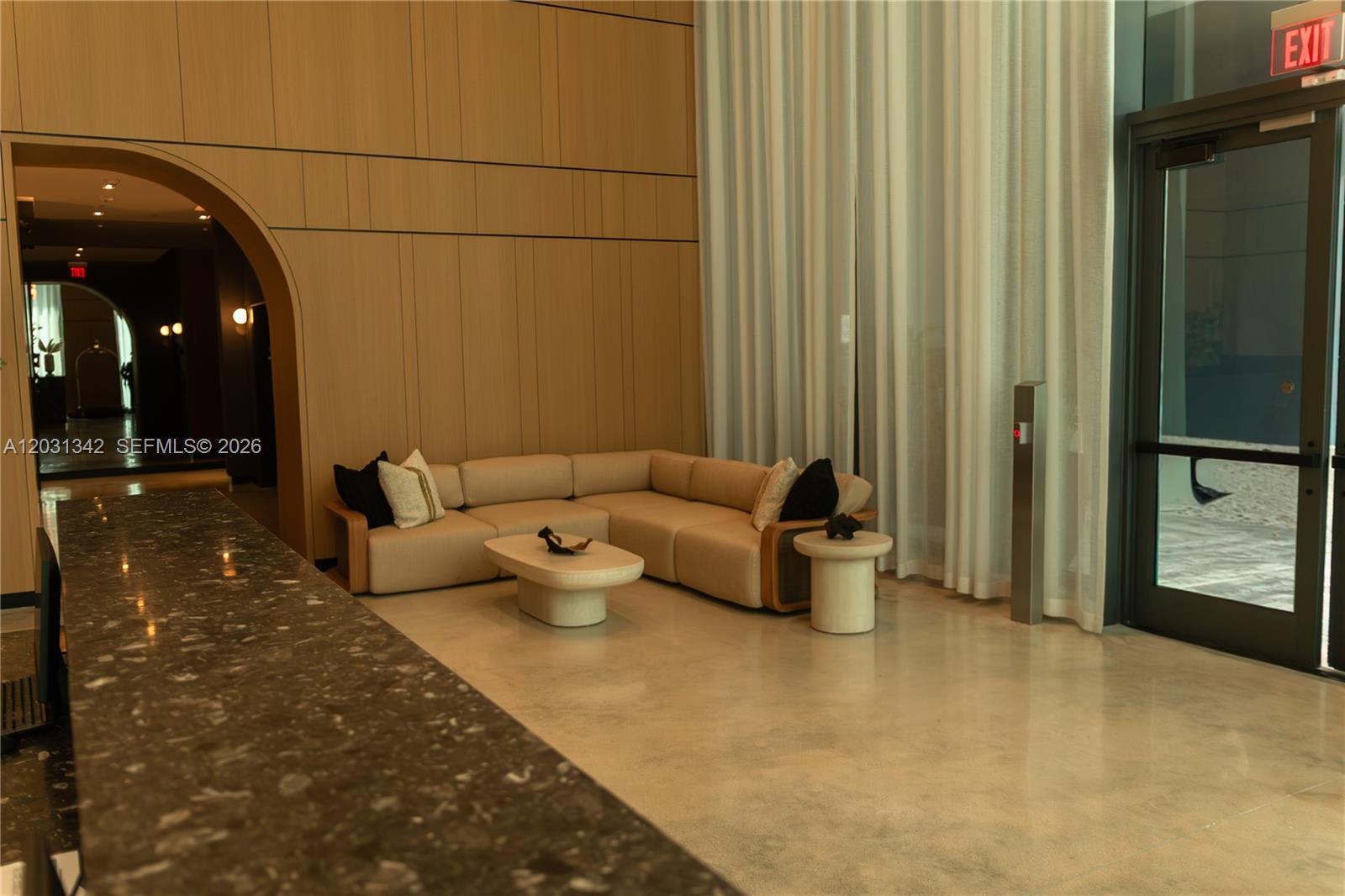 A modern lobby features a beige sectional sofa, a coffee table, and floor-to-ceiling curtains — 121 NE 5th St # 1012A, Miami FL 33132, MIAMI, FL
