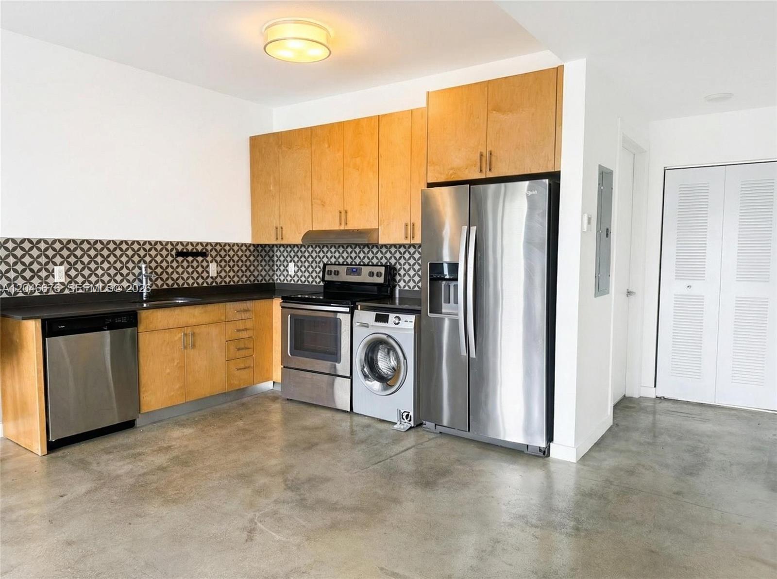 A kitchen features light wood cabinets, stainless steel appliances, a patterned backsplash, and concrete floors — 769 NW 1st St # 301, Miami FL 33128, MIAMI, FL