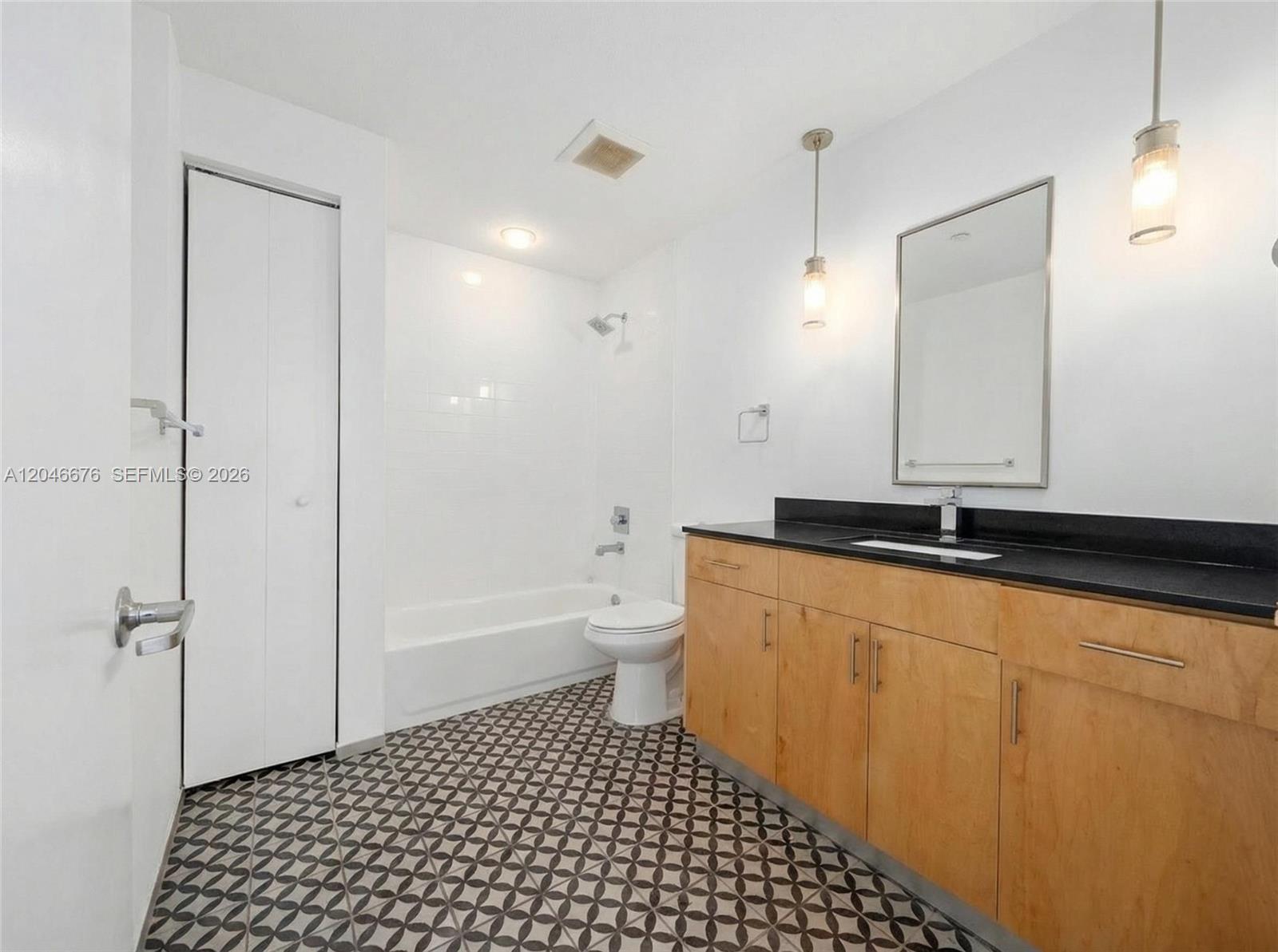 A bathroom features a wood vanity with a black countertop, a tub-shower, and patterned flooring — 769 NW 1st St # 301, Miami FL 33128, MIAMI, FL