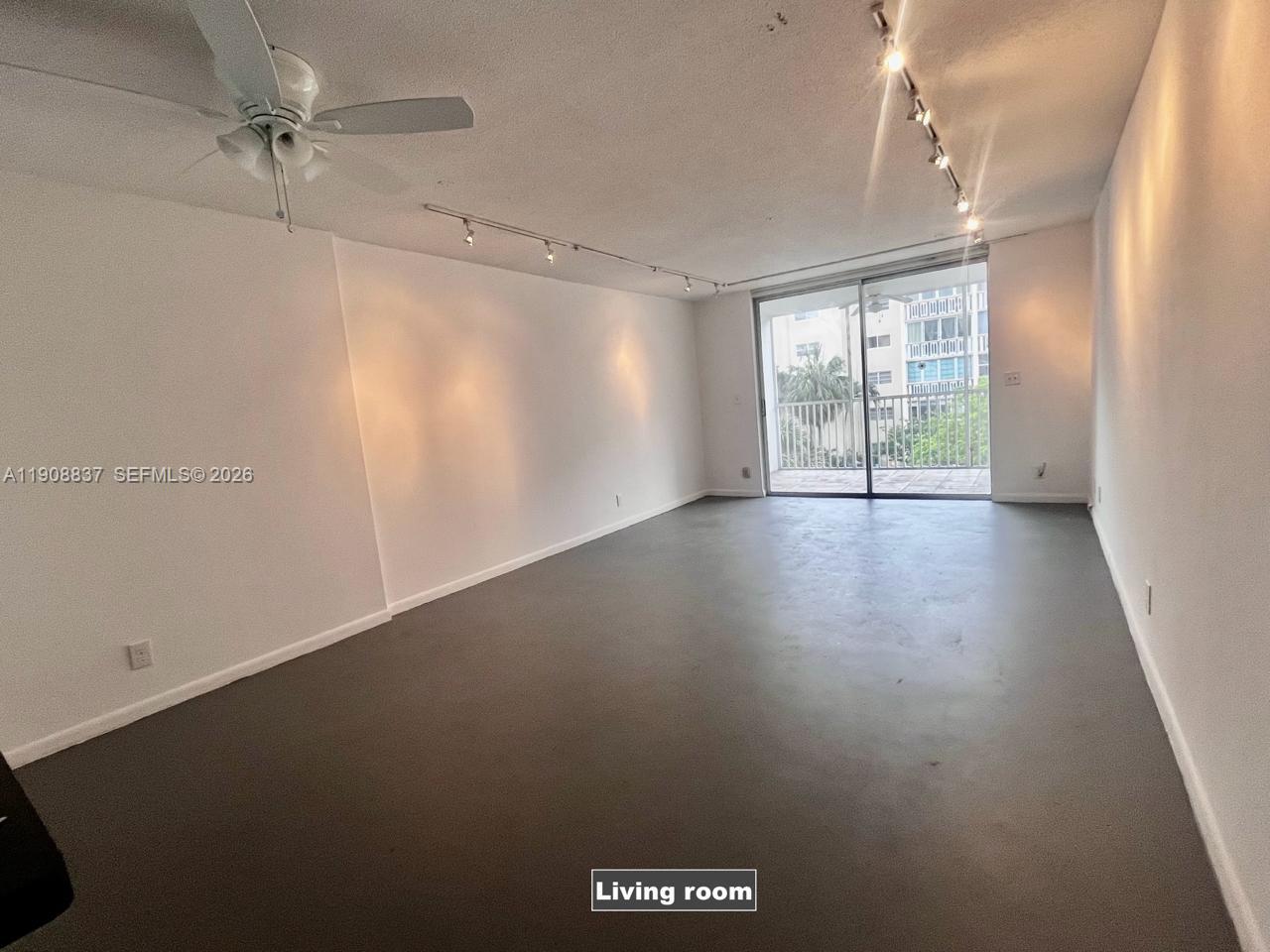 An empty living room features gray flooring, white walls, track lighting, and a sliding glass door — 619 NE 14th Ave # 304, Hallandale Beach FL 33009, HALLANDALE BEACH, FL