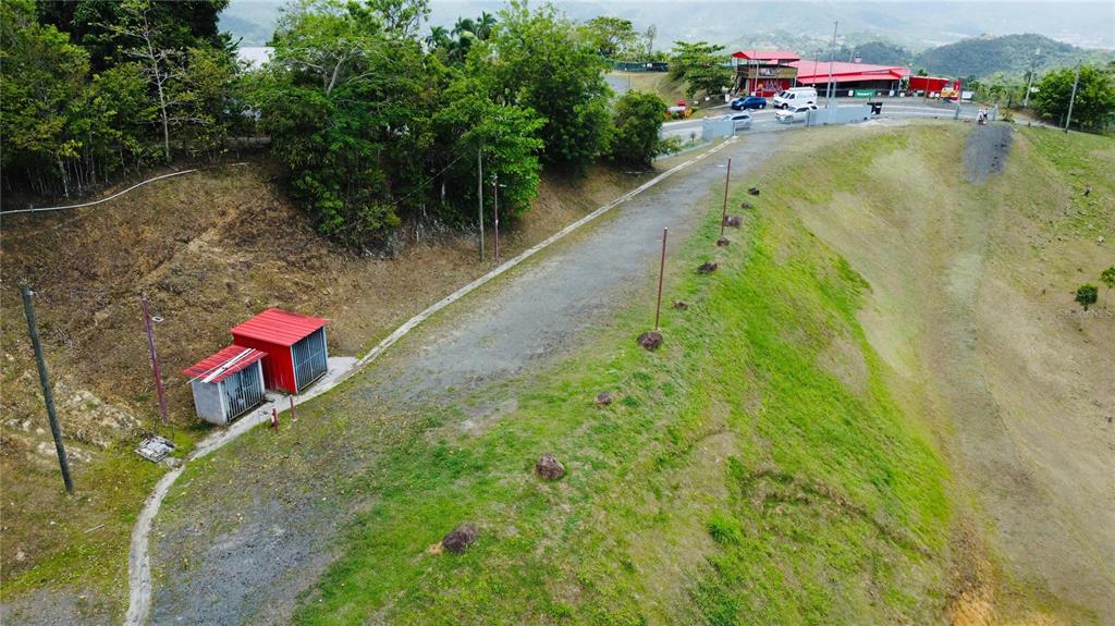 An aerial view shows a gravel path, a small utility structure, and a grassy hillside — BO. QUEMADO, SAN LORENZO, PR