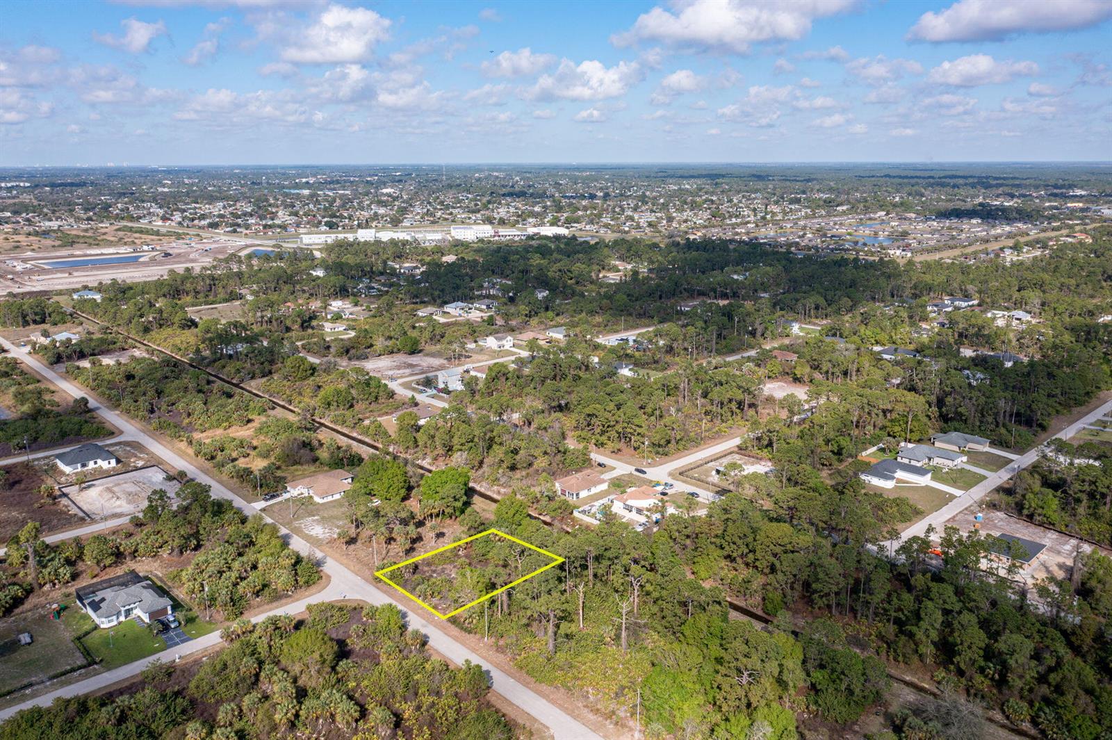 An aerial view shows a vacant, rectangular residential lot outlined in yellow near a road — 773 Cadis Street E, Lehigh Acres FL 33974, LEHIGH ACRES, FL