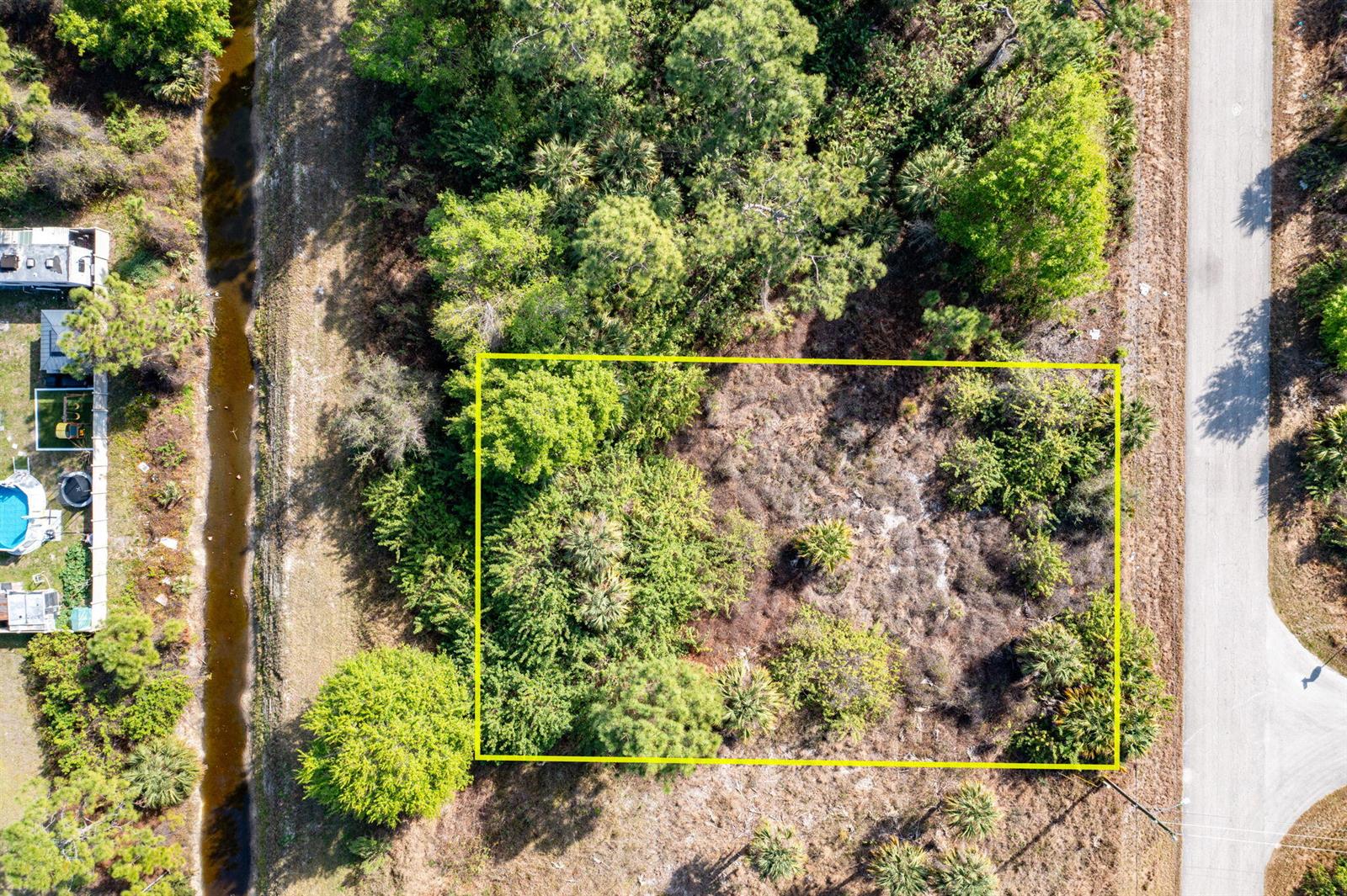An aerial view shows a rectangular, wooded vacant lot bordered by a road and canal — 773 Cadis Street E, Lehigh Acres FL 33974, LEHIGH ACRES, FL