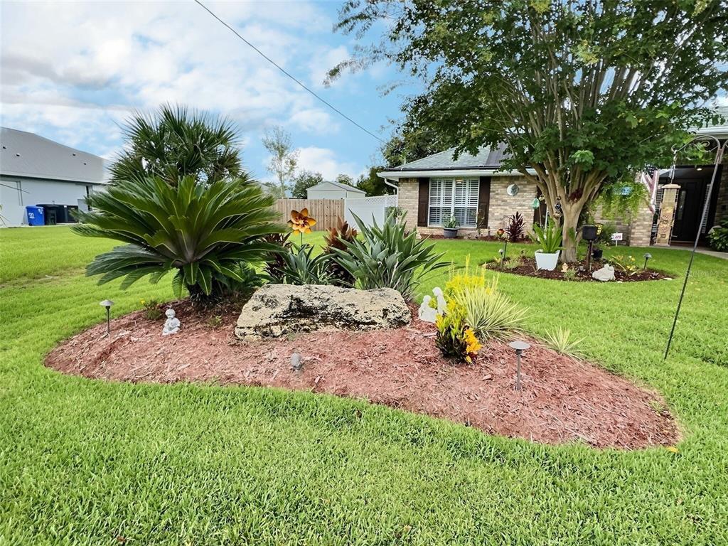 A front yard features a landscaped garden bed with a large rock and various plants — 28 FIELDING LANE, PALM COAST, FL