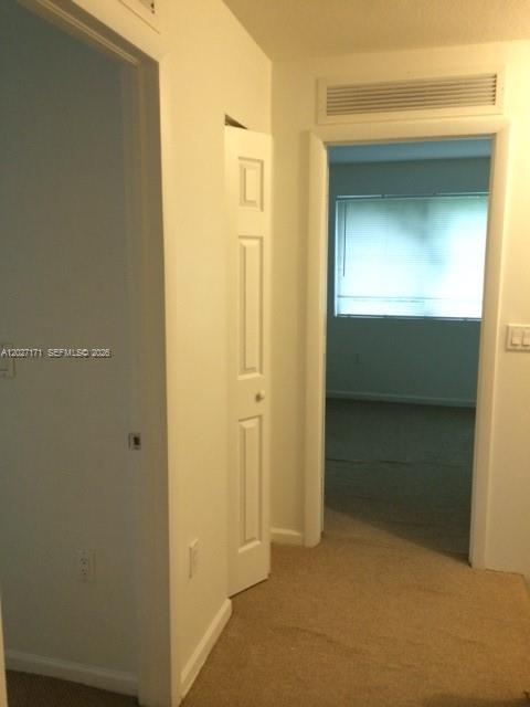 A hallway with beige carpet leads to a doorway revealing a room with a window — 1702 N 28th Ave # 1, Hollywood FL 33020, HOLLYWOOD, FL