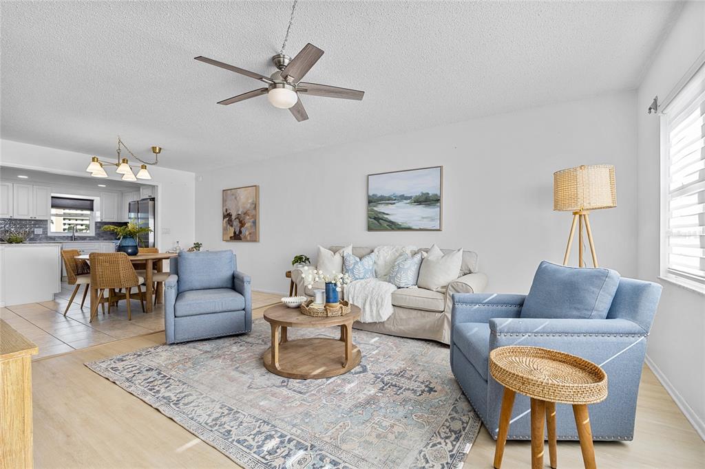 A living room features light wood floors, blue armchairs, a sofa, and a ceiling fan — 4775 COVE CIRCLE UNIT 203, ST PETERSBURG, FL