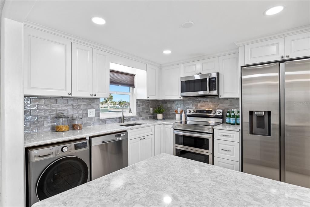 A modern kitchen features white cabinets, stainless steel appliances, a washer, and gray tile backsplash — 4775 COVE CIRCLE UNIT 203, ST PETERSBURG, FL